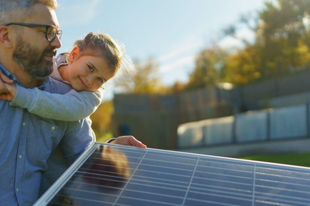 Father with his little daughter catching sun at solar panel,charging at their backyard. Alternative