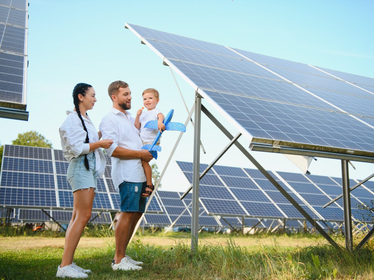 Young family with a small child in her arms on a background of solar panels.